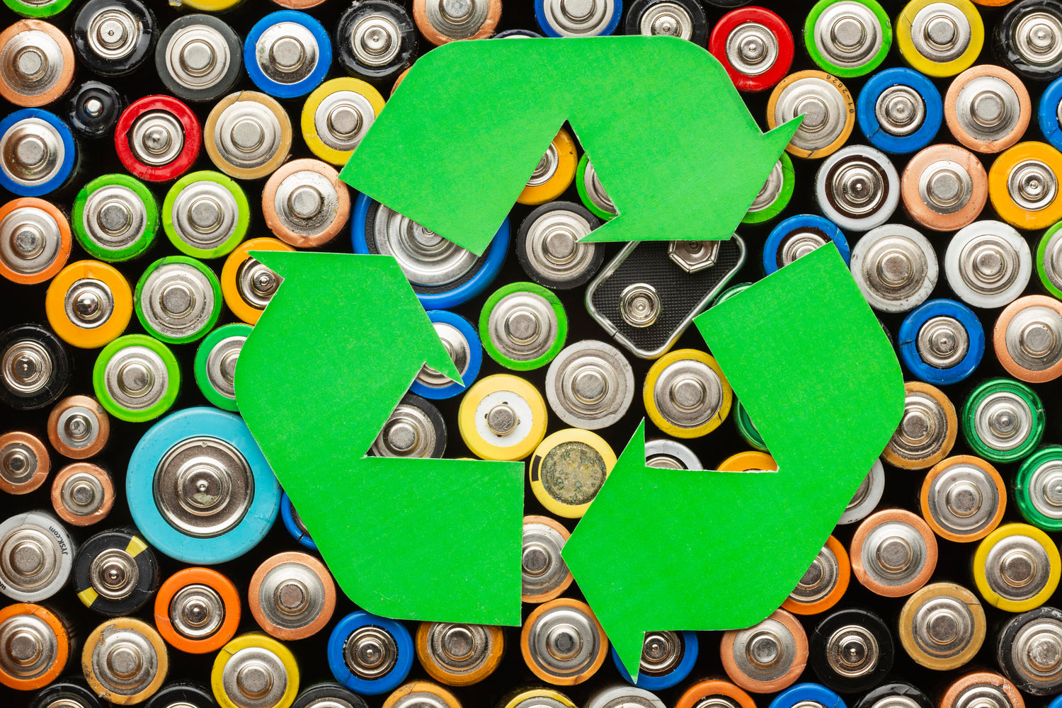 Green recycling symbol over a pile of used batteries.