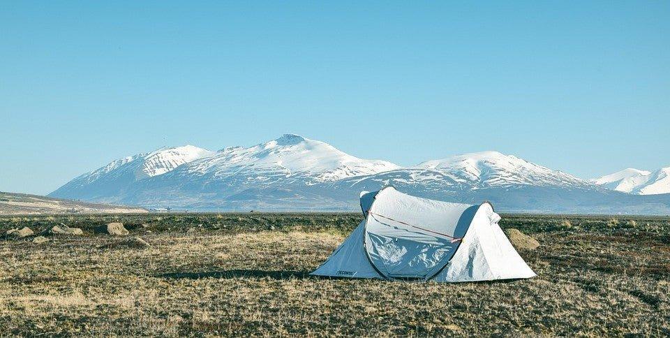 White camping tent in open field with snow-capped mountains, ideal for outdoor adventures and off-grid power needs.