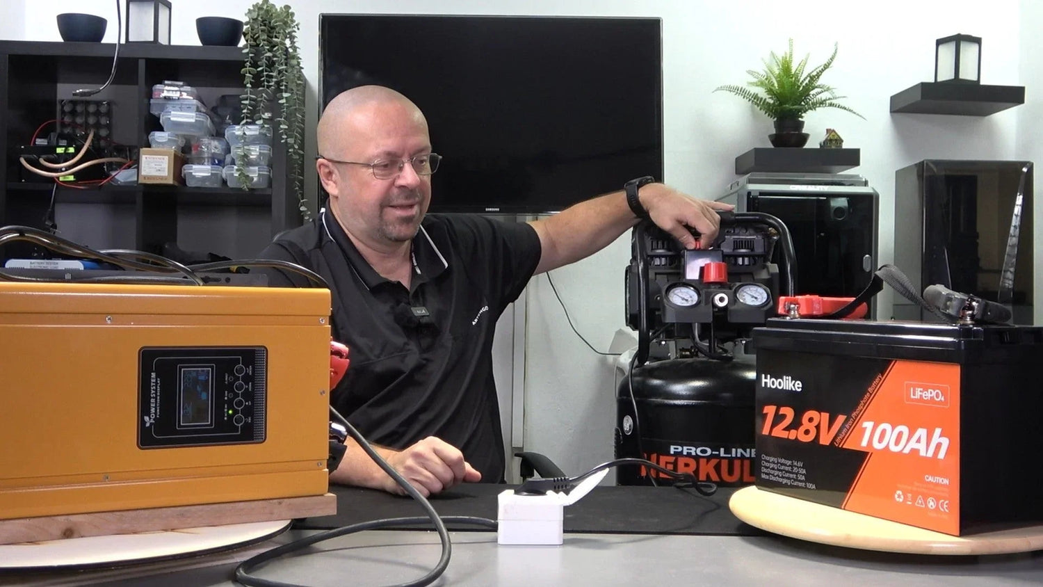 Man demonstrating 12.8V 100Ah LiFePO4 battery with power system and air compressor setup