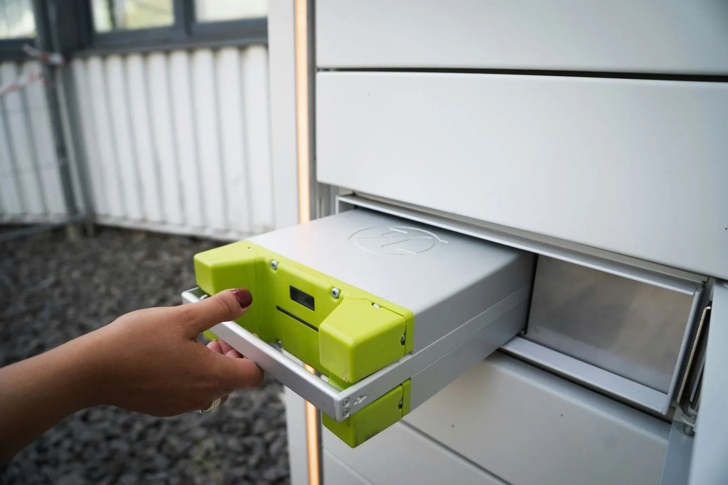 Hand installing a green LiFePO₄ battery module into a white energy storage unit outdoors