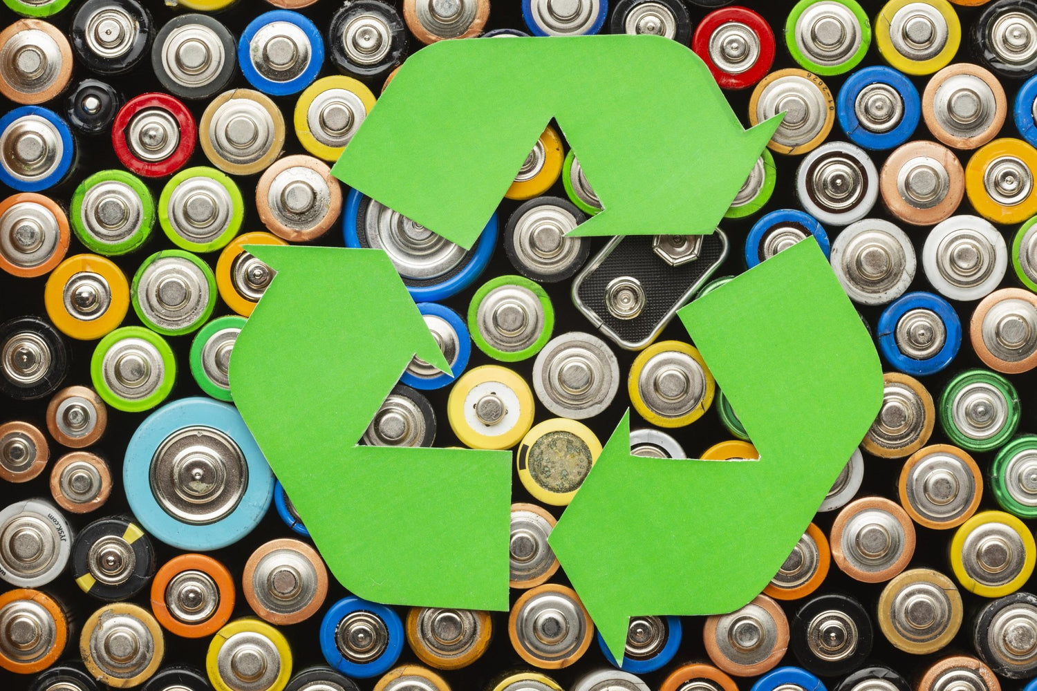 Green recycling symbol over a pile of used batteries.