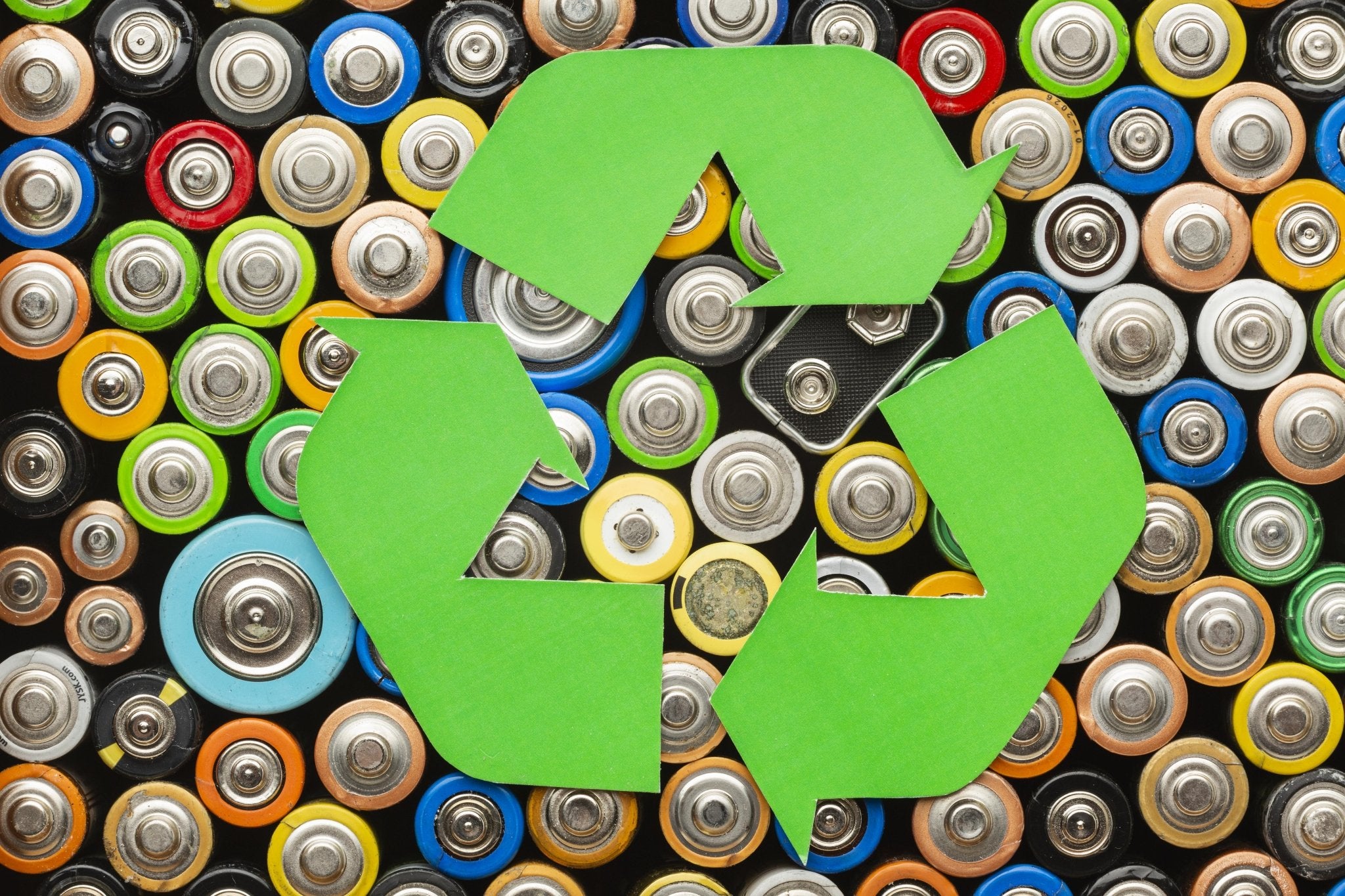 Green recycling symbol over a pile of used batteries.