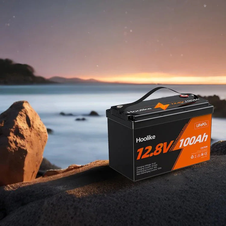 Hoolike 12.8V 100Ah LiFePO₄ battery on rocky shore at sunset, durable power for outdoor use