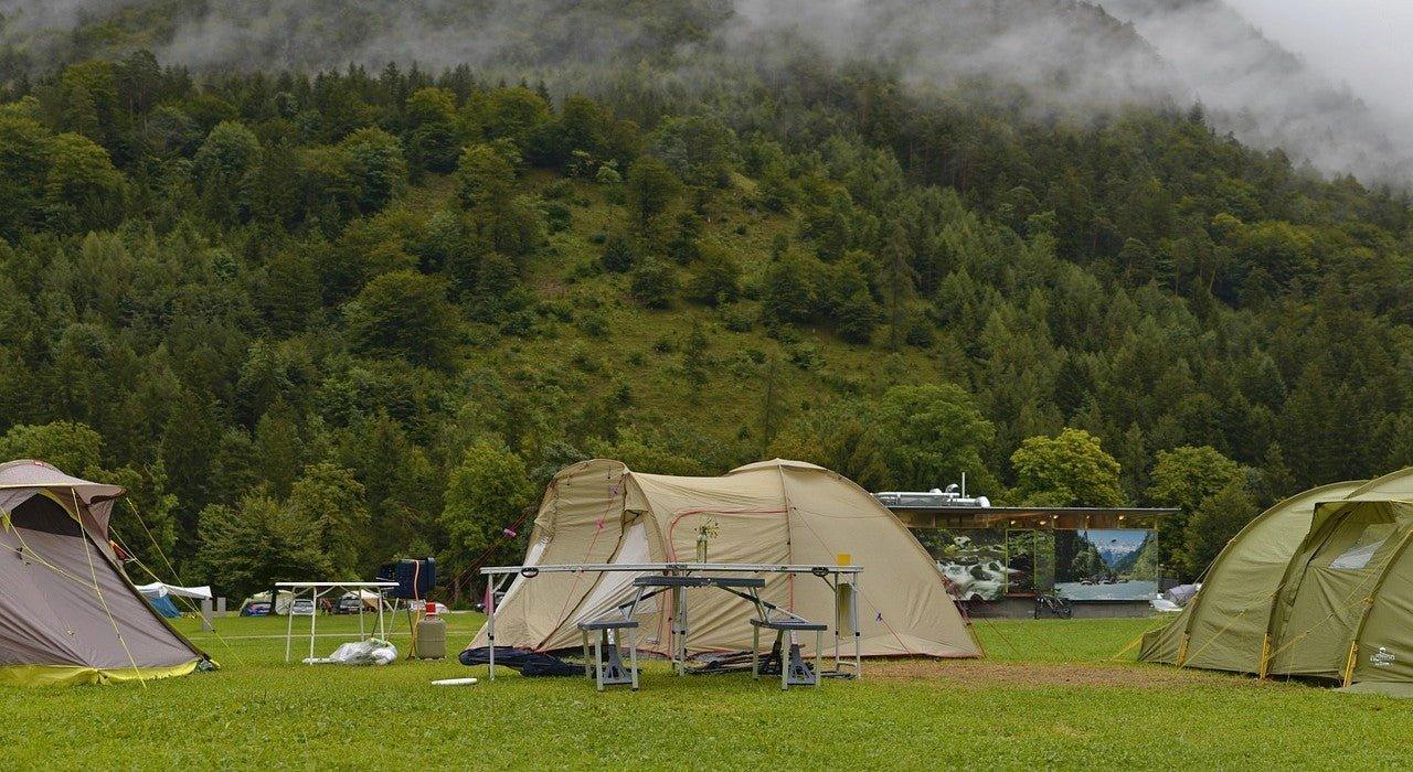 Camping tents set up in a lush green field with forested hills and misty mountains in the background.